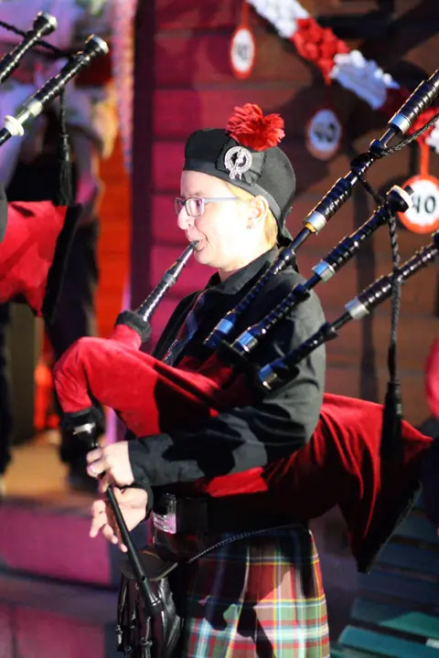 Dudelsackspieler mit rotem Dudelsack und Glengarry vor festlicher Kulisse